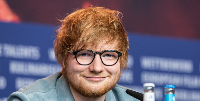 Ed wearing glasses and smiling with a microphone kept in front of him.