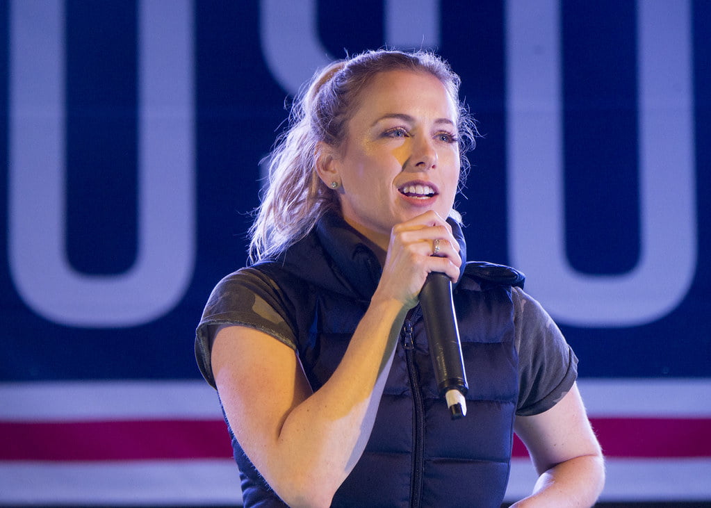Lliza Shlesinger, holding a mic, addressing people at a press conference