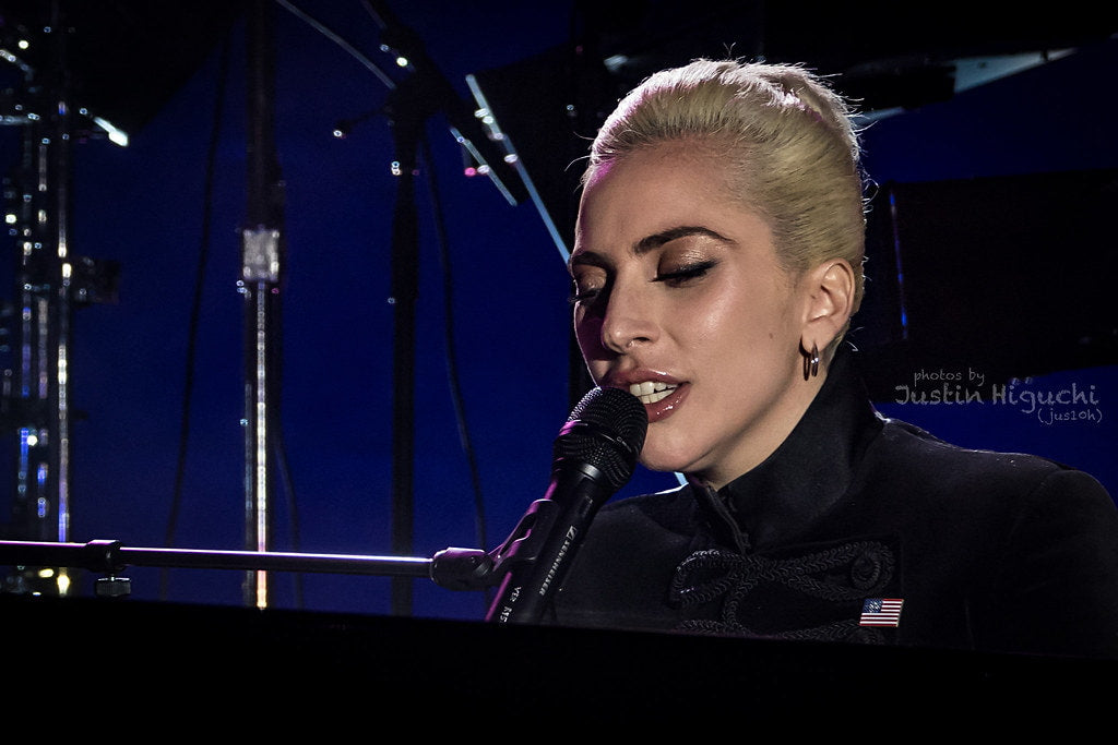 Lady Gaga sitting in front of a piano and singing at a concert