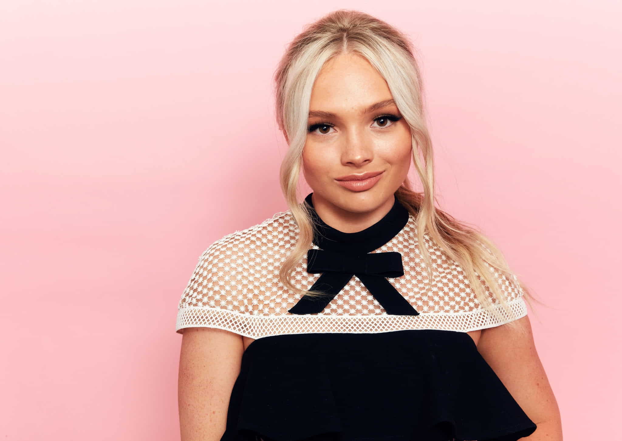 Natalie Alyn Lind in a black dress posing in front of a pink background