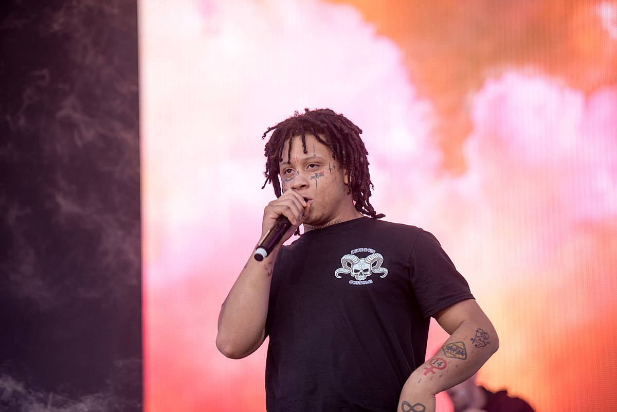 Trippie Redd striking a bold pose in vibrant streetwear, with a neon-lit background.