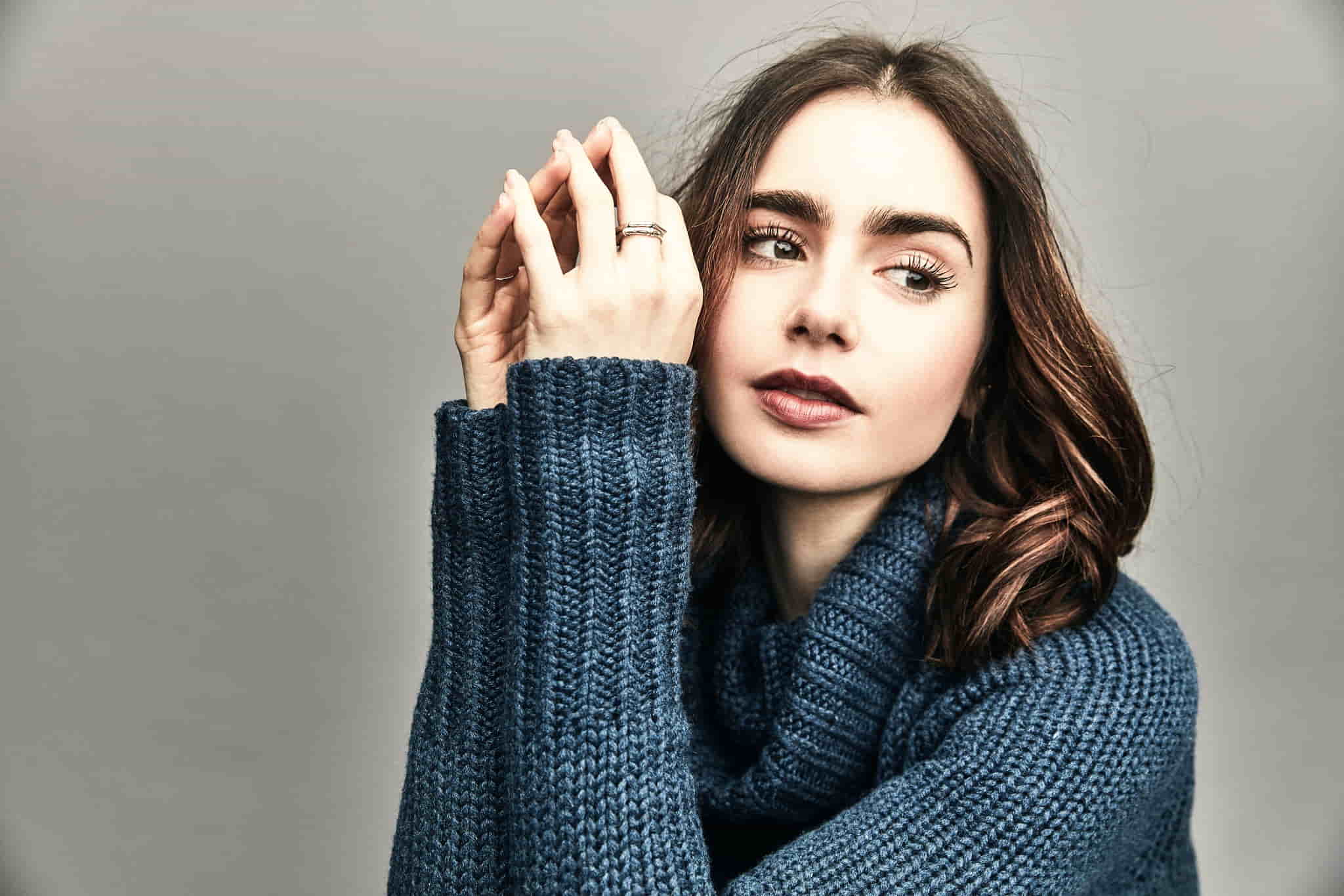 Lilly wearing a blue sweater, posing in front of a grey background.